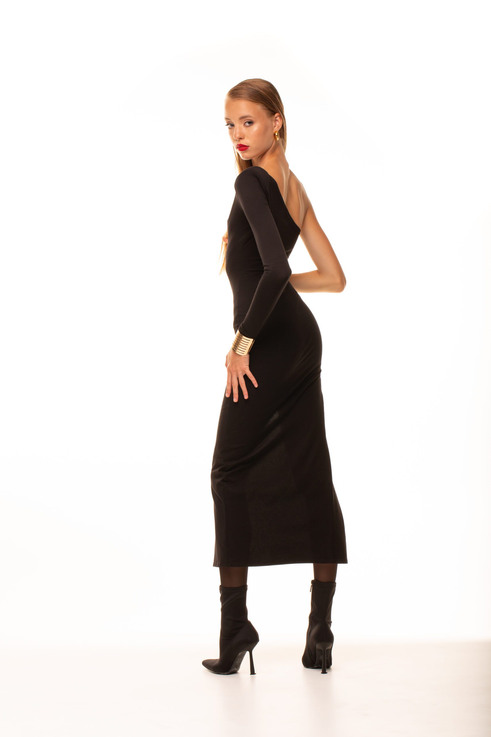 Дівчина у чорному платті LOREN DRESS від бренду Her Name стоїть на чорних каблуках спиною