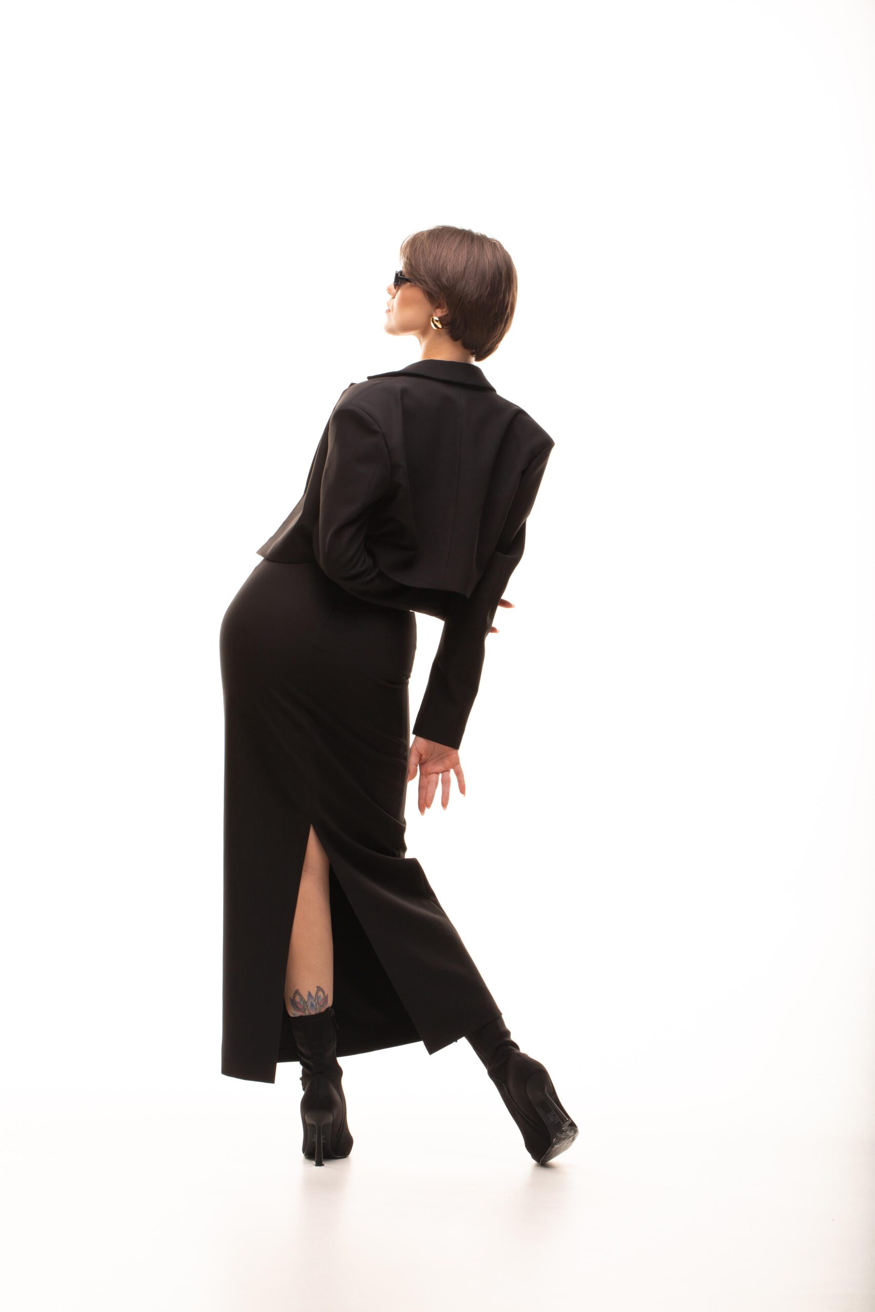 Дівчина у платті чорного кольору NFLUENCE SUIT (skirt) від бренду Her Name стоїть витягнувши праву руку на спиною