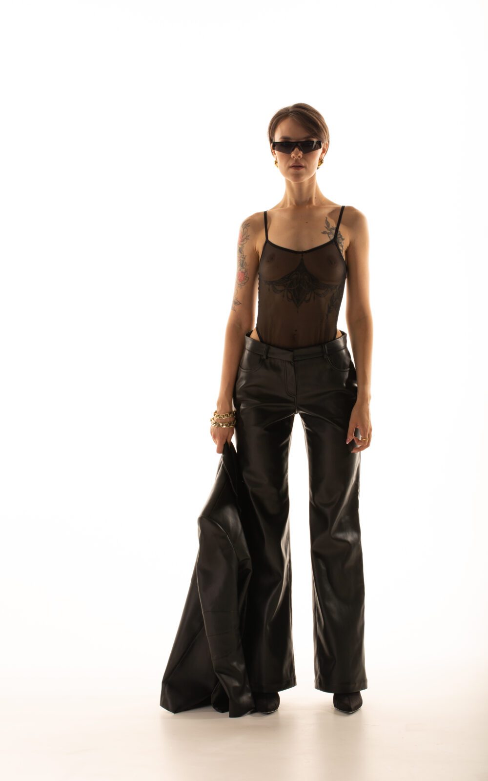 Дівчина у штанах LARA PANTS чорного кольору від бренду Her Name стоїть тримаючи чорний піджак у правій руці