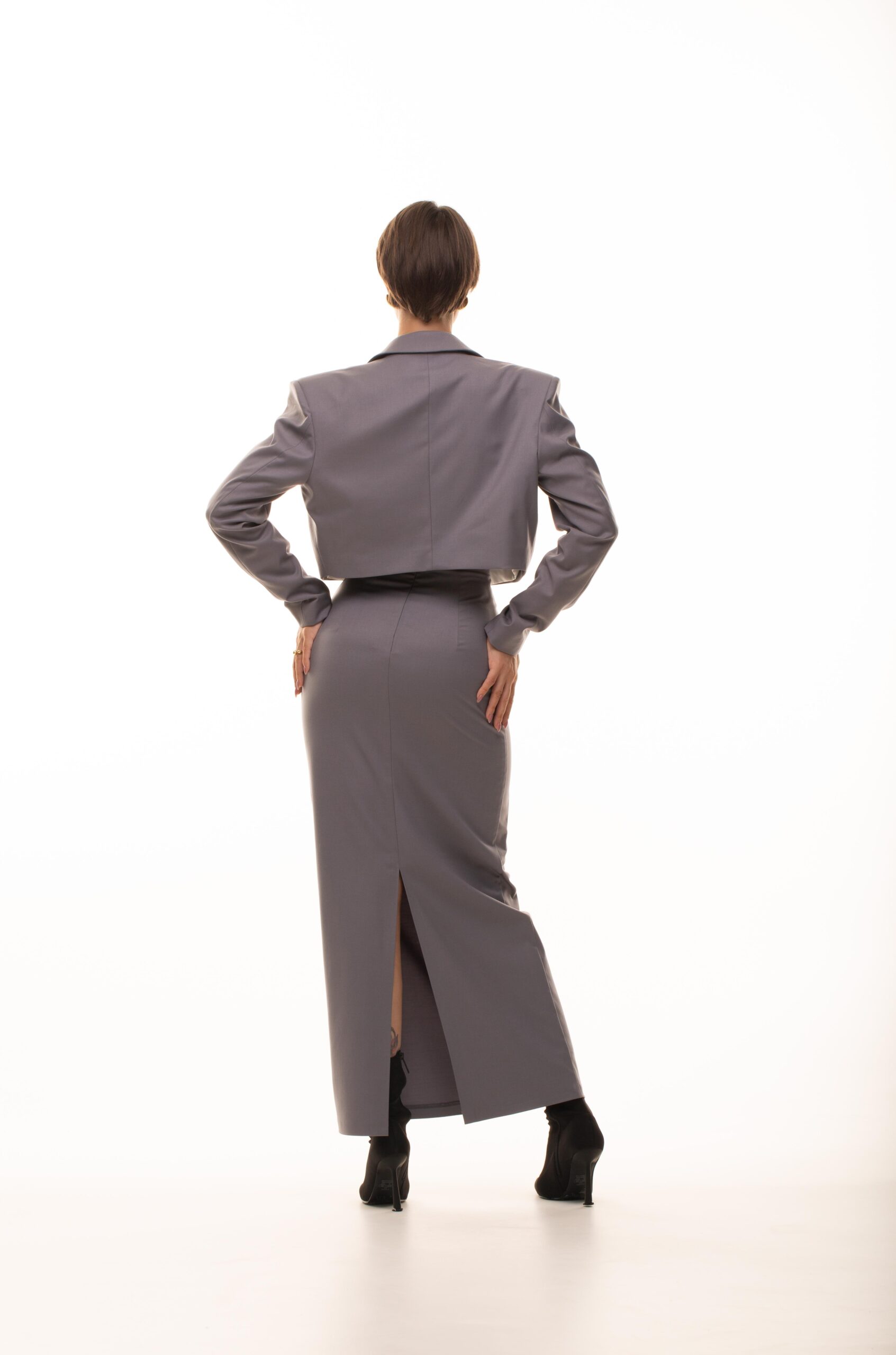 Дівчина у платті сірого кольору NFLUENCE SUIT (skirt) від бренду Her Name стоїть спиною поклавши дві руки за сідницю