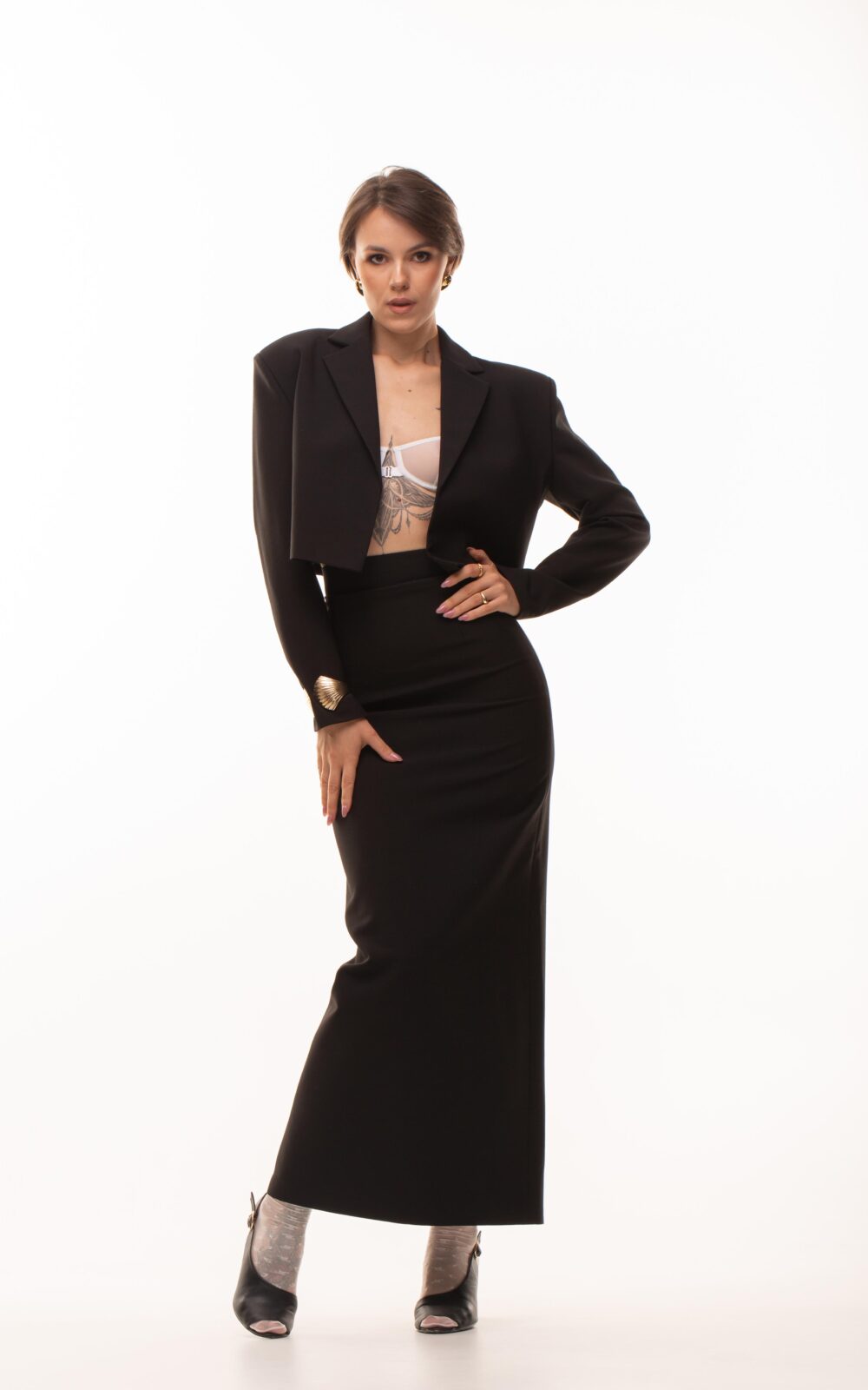 Дівчина у платті чорного кольору NFLUENCE SUIT (skirt) від бренду Her Name стоїть поклавши ліву руку на талію