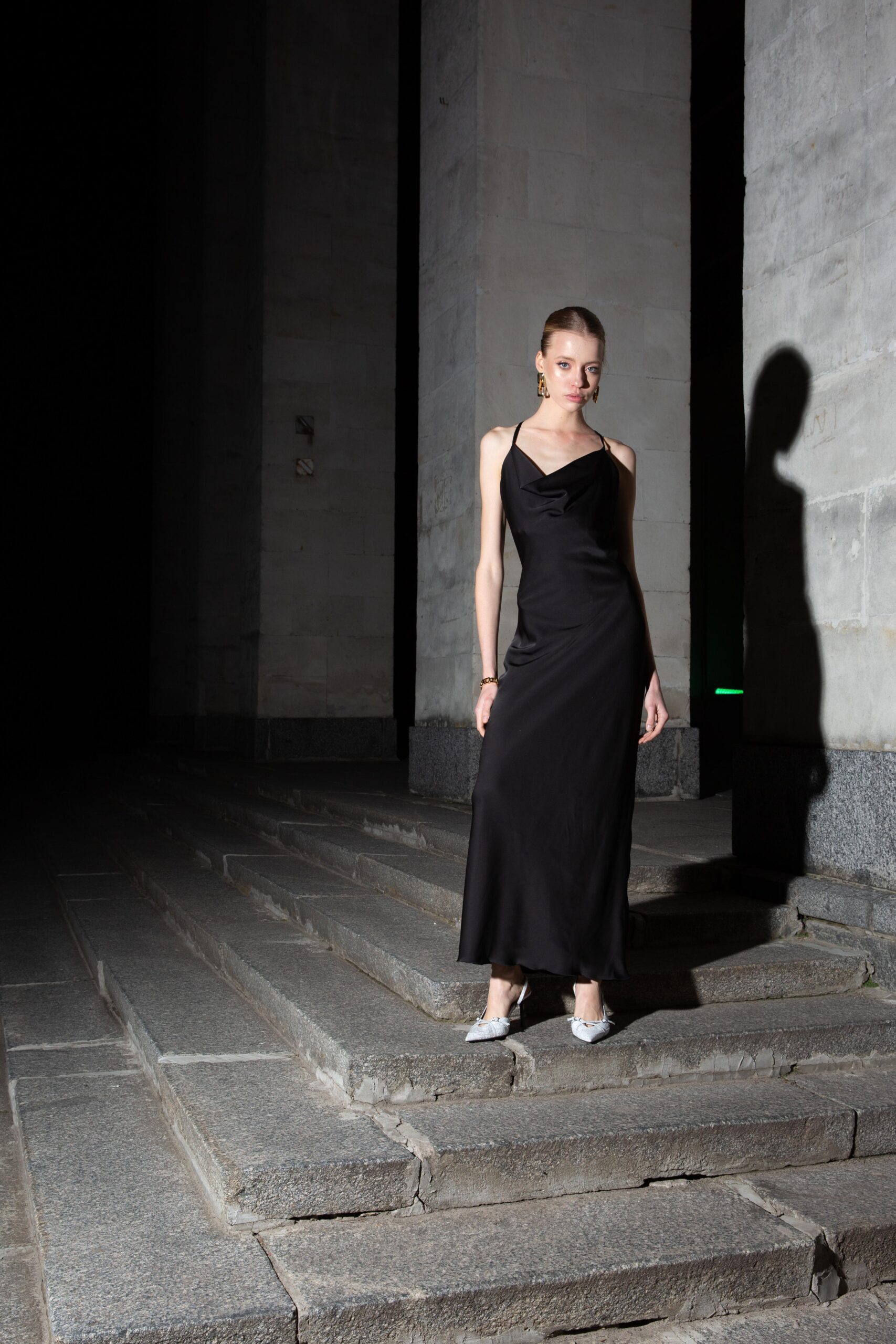 Дівчина у платті чорного кольору SLIP DRESS “LANA” від бренду Her Name стоїть