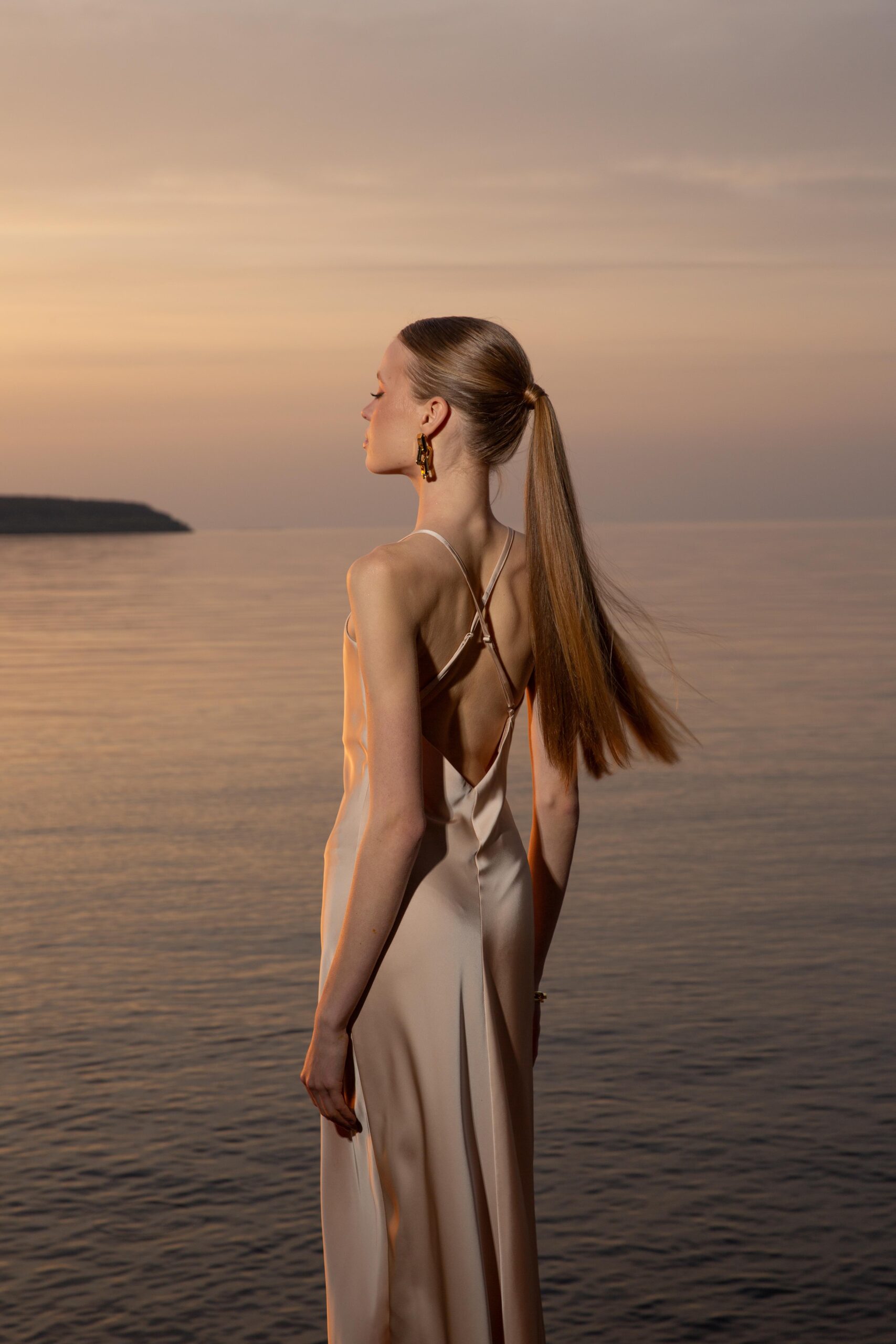 Дівчина у платті шампань кольору SLIP DRESS “LANA” від бренду Her Name стоїть боком на фоні Чорного моря