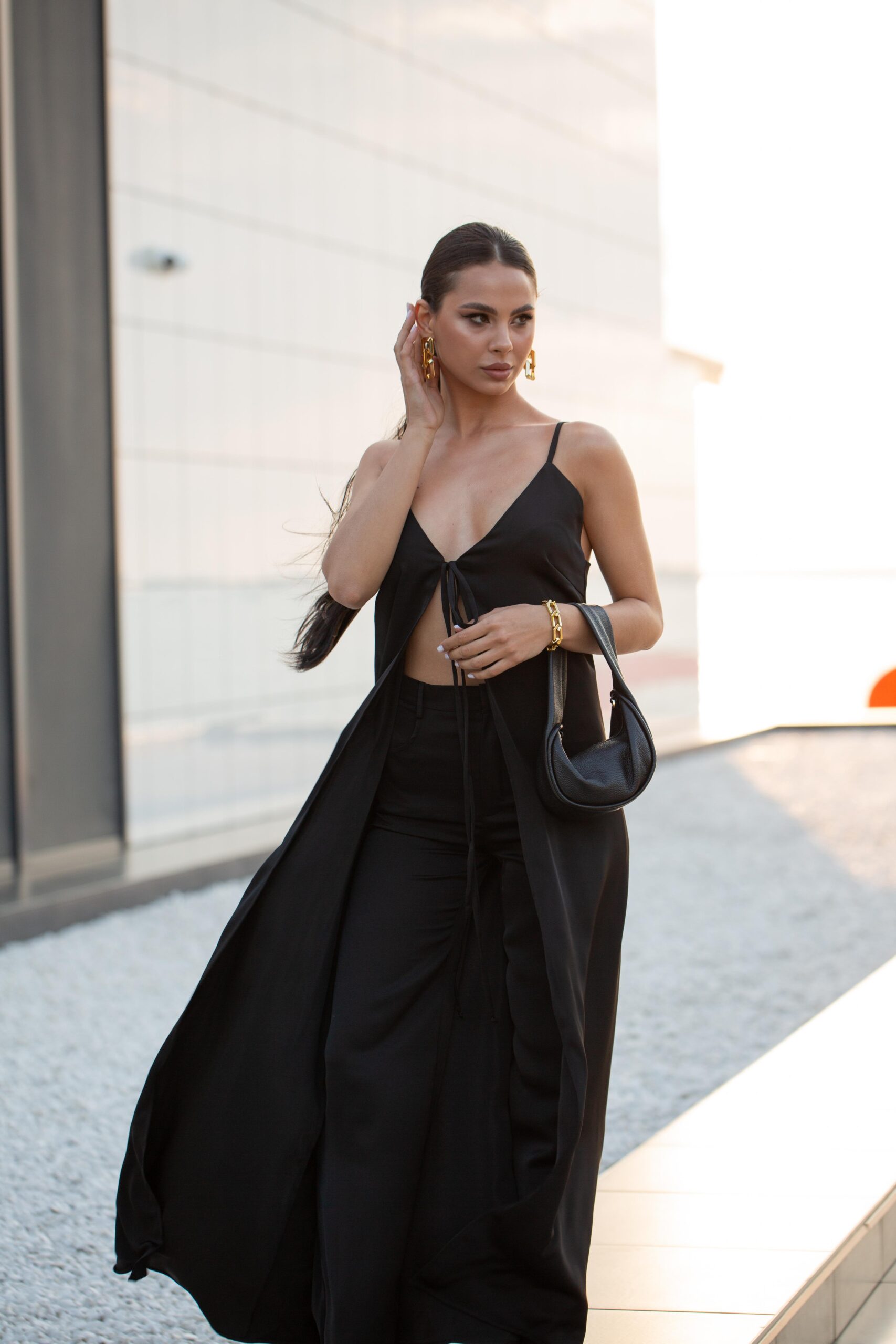 Модель у DOLCE SUIT чорного кольору від бренду Her Name стоїть на фоні стіни поправлючи правою рукою волосся