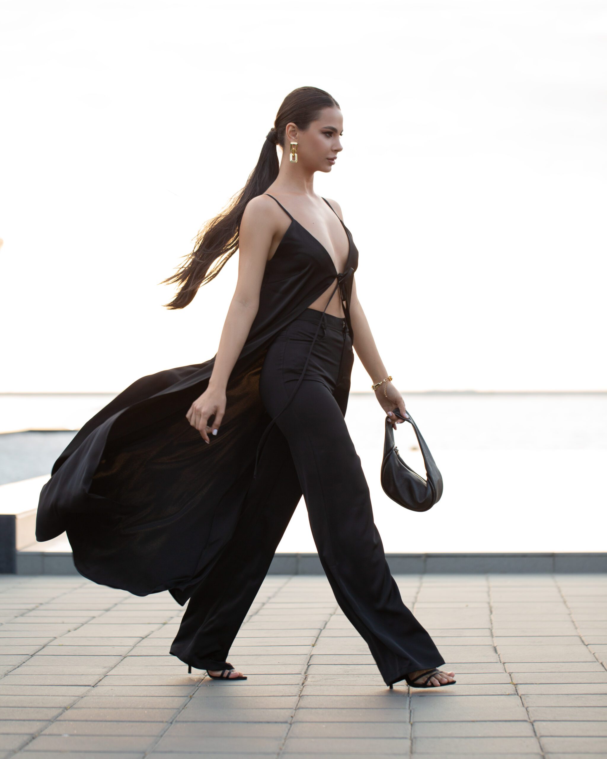 Модель у DOLCE SUIT чорного кольору від бренду Her Name іде по набережній на фоні моря